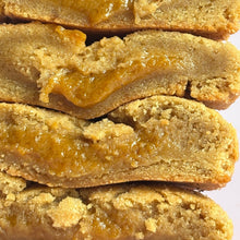 Load image into Gallery viewer, Four golden-brown sugar cookies stacked vertically, sliced open to reveal a thick, glossy caramel or orange filling running through the center.
